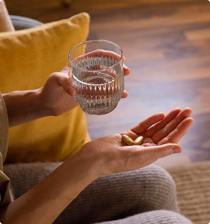 Hands holding a glass of water and two capsules